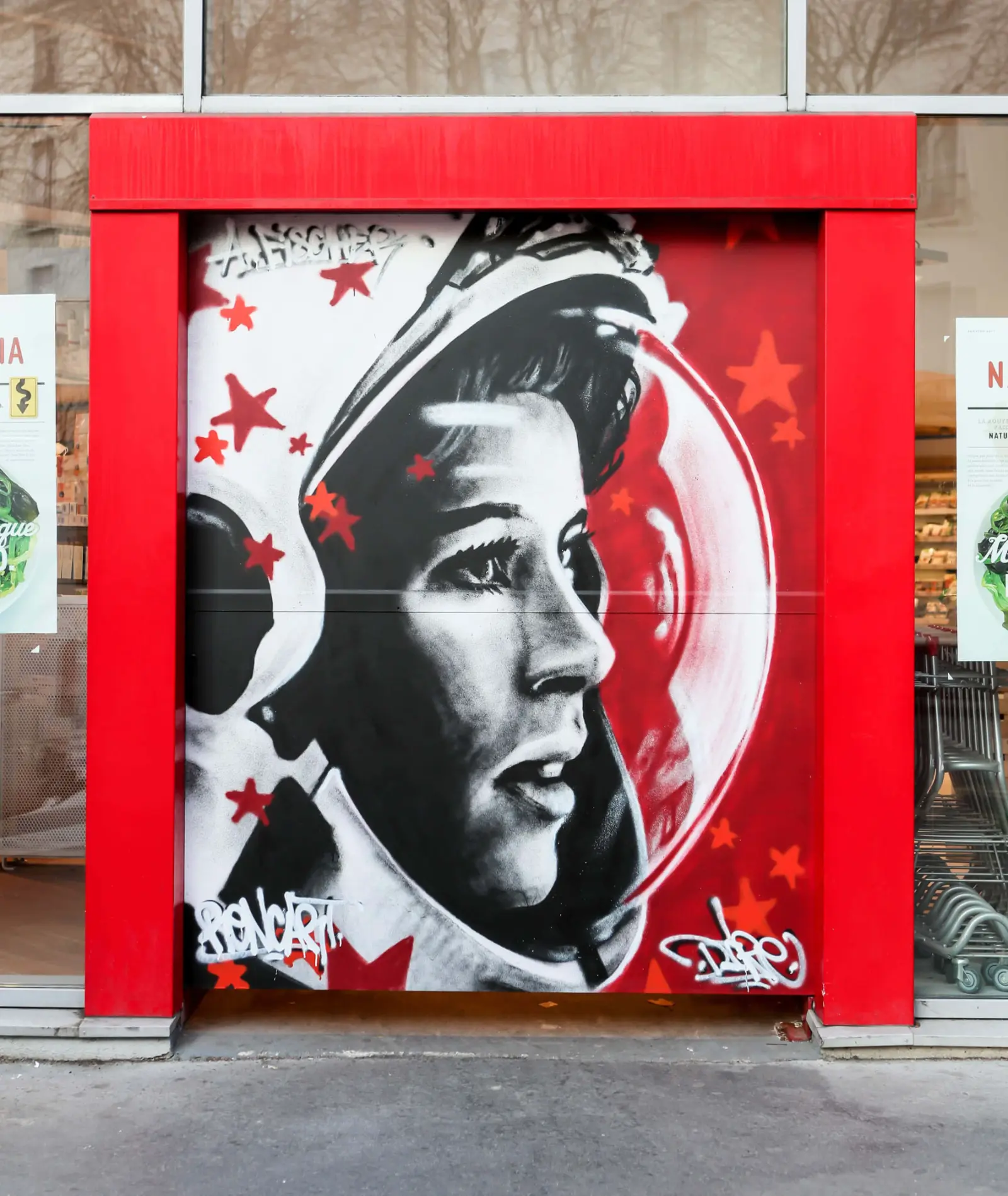 Fresque pochoir noir et rouge d'une cosmonaute sur la devanture Naturalia — rue Crozatier, Paris